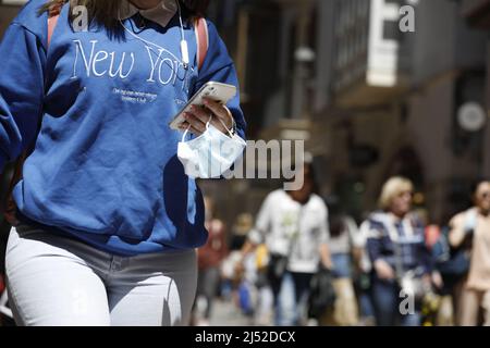 Palma, Spanien. 19. April 2022. Eine Frau trägt ihre medizinische Maske am Handgelenk, während sie in der Innenstadt von Palma de Mallorca spazieren geht. In Spanien müssen Sie ab morgen, Mittwoch, den 20. April, fast überall keine Corona-Schutzmaske mehr tragen. Auf Mallorca ist das Tragen einer Maske jedoch weiterhin in allen öffentlichen Verkehrsmitteln, Gesundheitseinrichtungen wie Gesundheitszentren, Krankenhäusern oder Apotheken Pflicht. Quelle: Clara Margais/dpa/Alamy Live News Stockfoto