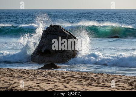 Am Garapatta State Beach, CA, ergattert eine Welle gegen einen Felsen bei Sonnenuntergang Stockfoto