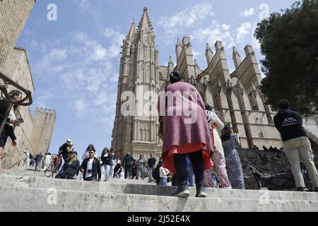 Palma, Spanien. 19. April 2022. Die Menschen gehen neben der Kathedrale von Palma de Mallorca. In Spanien wird ab Mittwoch, dem 20. April, fast nirgendwo eine Corona-Schutzmaske getragen werden müssen. Allerdings wird in Mallorca noch eine Maske in allen öffentlichen Verkehrsmitteln, Gesundheitseinrichtungen wie Gesundheitszentren, Krankenhäusern oder Apotheken tragen müssen. Quelle: Clara Margais/dpa/Alamy Live News Stockfoto