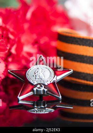 Russland, Moskau, Februar 2022. Victory Day Mai 9 Feiertagshintergrund Komposition, sowjetische Ordnung, Nelke, St. George Band, schwarzer Hintergrund. Stockfoto