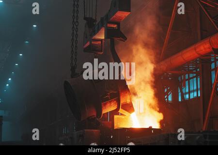 Metall, das mit Funken ausströmt. Schmelzen von Gusseisen-Teilen in der Gießerei. Metallurgische Anlage oder Stahlwerk. Stockfoto