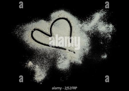Schwarzer Hintergrund bestreut mit Mehl Herzform, geschmiertes Mehl, Tisch zum Kochen, Teig Rollen. Vorbereitung für das Backen, Draufsicht isoliert auf einem schwarzen Stockfoto