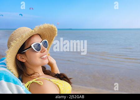 Porträt einer lächelnden Frau in Strohhut und Sonnenbrille, die sich auf der Sonnenliege entspannt Stockfoto