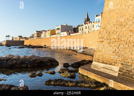 Schöne Städte in Sardinien - bunte Häuser in der Altstadt von Alghero über der Festungsmauer am Meer in der warmen Abendsonne, Italien Stockfoto