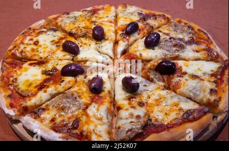 Köstliche Pizza mit Oliven Pilze Pepperoni Tomaten Käse Kräuter liegt in Scheiben geschnitten auf einem Holzblech Stockfoto