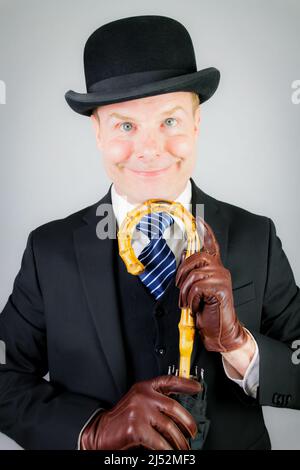 Porträt eines britischen Geschäftsmannes in dunklem Anzug und Lederhandschuhen mit Regenschirm. Vintage Style von eleganten englischen Gentleman Stereotyp. Stockfoto