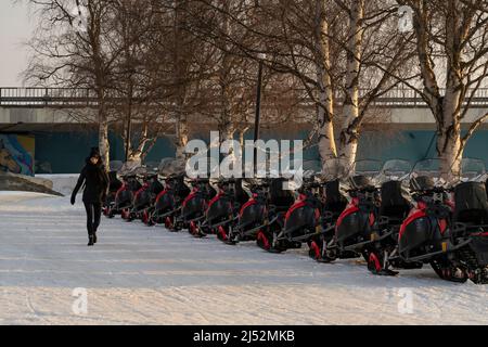 Rovaniemi, Finnland - 18.. März 2022: Schneemobile, die im Morgengrauen an einer schneebedeckten Straße in Rovaniemi, Finnland, geparkt sind. Stockfoto