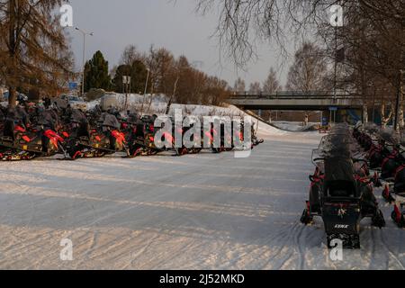 Rovaniemi, Finnland - 18.. März 2022: Schneemobile, die im Morgengrauen an einer schneebedeckten Straße in Rovaniemi, Finnland, geparkt sind. Stockfoto