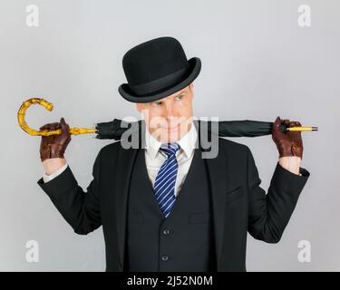 Porträt eines britischen Gentleman in dunklem Anzug und Regenschirm mit Bowler-Hut. Konzept des Action Hero Retro Spy Stockfoto