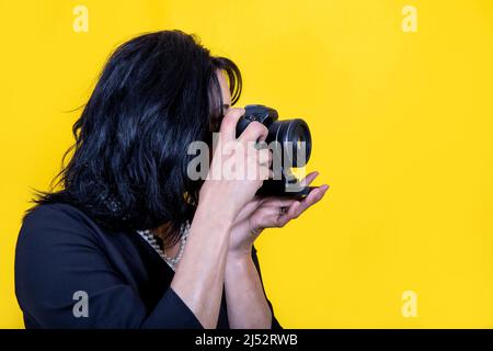 Junge Frau macht ein Foto. Die schöne Brünette Frau trägt eine schwarze Jacke und eine Perlenkette und hält die Kamera in der Hand. Stockfoto