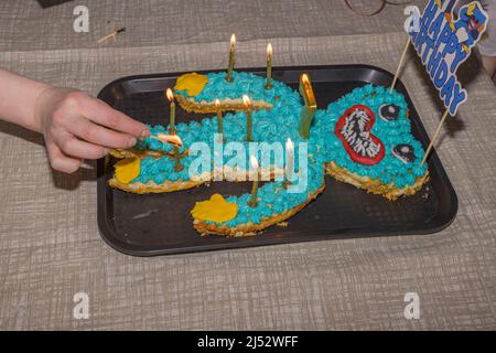 Menschenhand zündet Kerzen in einem Kuchen an, um den Geburtstag des Kindes zu feiern. Schweden. Stockfoto