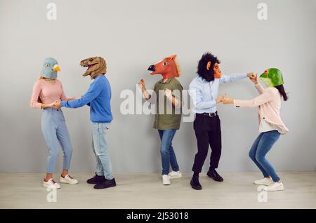 Fröhliche, exzentrische junge Menschen mit Köpfen verschiedener Tiere tanzen und haben gemeinsam Spaß. Stockfoto