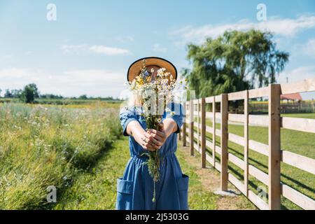 Bauernhöfe und Touren auf dem Bauernhof, Wochenendausflug auf dem Bauernhof Cottagecore. Farm Trips Für Ein Ruhiges Wochenende. Eine Frau in rustikalem Kleid und mit Wildblumen vor Stockfoto