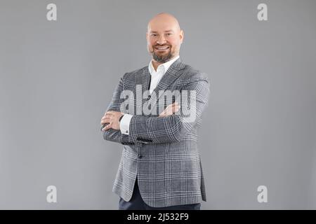Porträt eines fröhlichen Geschäftsmannes mittleren Alters in grauer karierter Jacke, Weste, weißem Hemd, stehend mit gekreuzten Armen. Stockfoto
