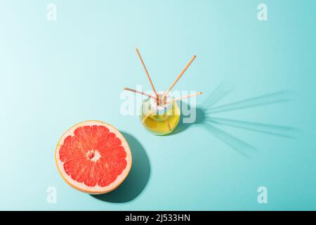 Glasflasche mit Aroma-Diffusor und roter Grapefruit auf hellblauem Hintergrund. Harte Schatten, Draufsicht Stockfoto