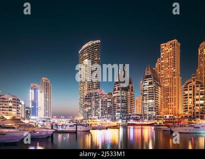 Dubai Marina Port, VAE, Vereinigte Arabische Emirate. Steg Mit Vielen Festgetäuten Yachten, Sightseeing-Boot In Der Abendnacht Illuminationen. Nachtansicht Von Dubai Stockfoto