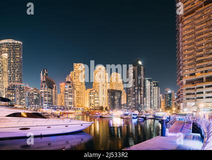 Anlegesteg Mit Vielen Festgetäuten Yachten Bei Abendlichen Illuminationen. Blick Auf Die Skyline Von Dubai Marina Bei Nacht Stockfoto