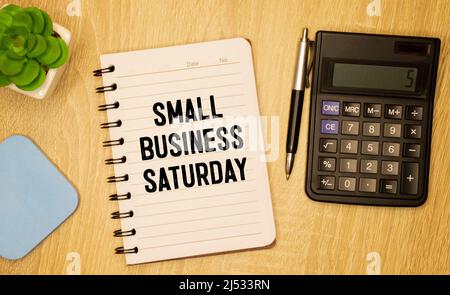 Text Small Business Saturday in Notebook auf weißem Tisch mit Office-Tools Stockfoto