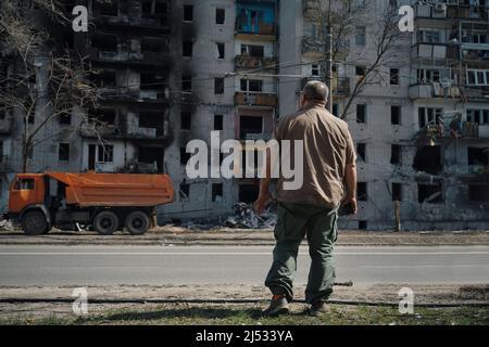 Ein Mann steht in der Nähe eines zerstörten Hauses, das von einer Granate aus militärischen Operationen in der Ukraine getroffen wurde Stockfoto