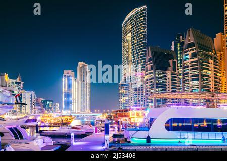 Nachtansicht des Wolkenkratzers in Dubai Marina und Boote, Yachten, die in der Nähe des Pier in der Abendnacht festgemacht wurden Stockfoto