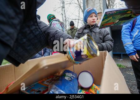 Iwankiv, Oblast Kiew, Ukraine. 19. April 2022. Kinder sammeln Lebensmittel und Spielzeug von der humanitären Hilfskruppe New Format 20 in einem Dorf in Iwankiv im Kiewer Gebiet. Die ukrainischen Streitkräfte haben die Stadt Anfang April zurückeroberte. Die russische Besatzung hat große Verwüstungen von Grundstücken verursacht und die Nahrungsmittelversorgung in ländlichen Gebieten erschwert. (Bild: © Daniel Ceng Shou-Yi/ZUMA Press Wire) Stockfoto