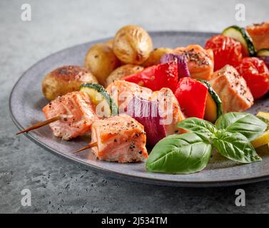 Teller mit gegrillten Lachsspießen und Gemüse auf grauem Tisch aus nächster Nähe Stockfoto