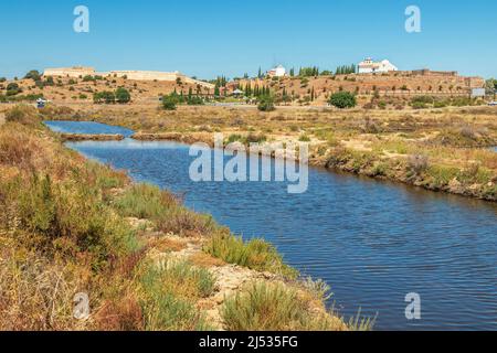 Salzpfannen im Vordergrund und im Hintergrund die Festung, die Mühle und die Kirche von Castro Marim an der Algarve, Portugal, an einem sonnigen Sommertag Stockfoto