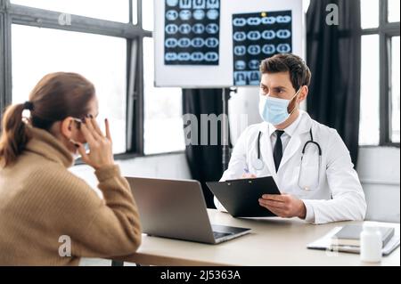 Konsultation mit einem Arzt in einer Klinik. Kaukasische Allgemeinmedizin Arzt in einer medizinischen Uniform und Schutzmaske, berät den Patienten, verschreibt Behandlung, hört auf Beschwerden, gibt Ratschläge Stockfoto