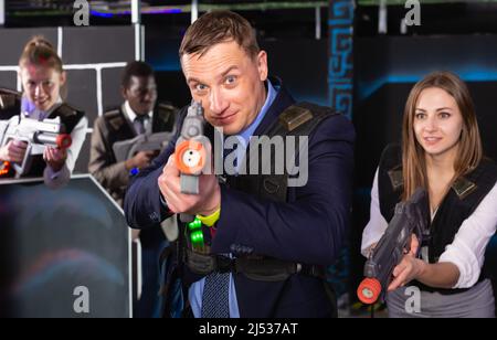 Fröhlicher Mann und seine Kollegen im Laser-Tag-Raum Stockfoto