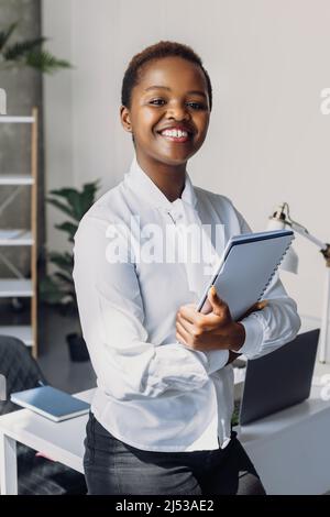 Porträt einer erfolgreichen Afro-Geschäftsfrau, die Dokumente hält und lächelt, während sie in der Küche steht. Porträt einer Geschäftsfrau. Büro Stockfoto