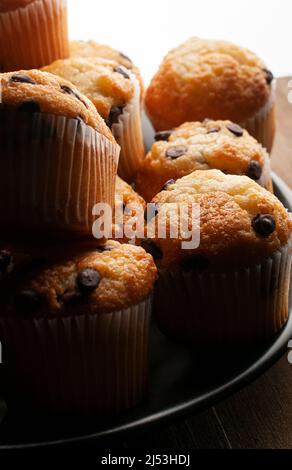 Chiaroscuro oder dunkle Makrofotografie, Vanille-Cupcakes mit Schokoladenstückchen auf einem schwarzen Teller, Konzept der hausgemachten Speisen Stockfoto