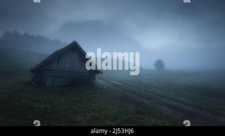 Nebliger Morgen mit einer Hütte und Bergen im Hintergrund Stockfoto