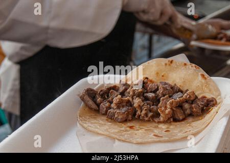 Street Food Fotografie, ein Carne Asada Taco auf einem Teller, mexikanisches kulinarisches Kulturkonzept. Ein Taco steht auf der Straße. Stockfoto