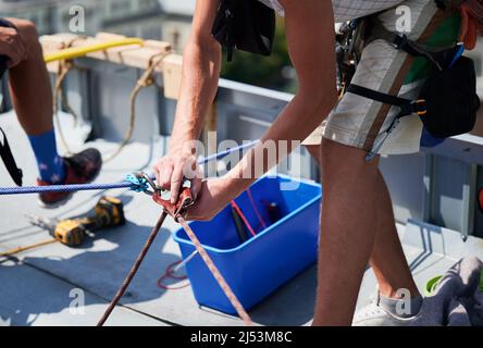 Arbeiter beim Bergsteigen waschen Glasfenster des Hochhauses. Nahaufnahme des Reinigungsers, der mit Kletterseilen auf dem Dach des Wolkenkratzers arbeitet. Stockfoto