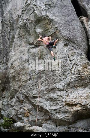 Junger Mann klettert schwierige Route auf einem hohen Felsen mit Seil. Furchtlose Kletterer trainieren am Sommertag Klettern. Konzept für Extremsport, Abenteuer und aktiven Lebensstil. Stockfoto