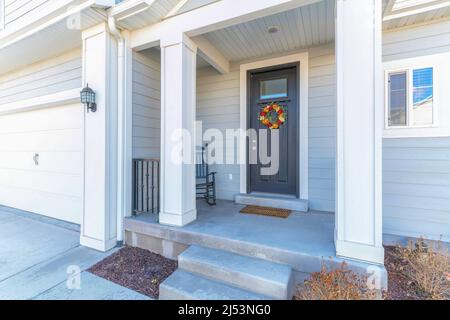 Haus Veranda mit Schaukelstuhl in der Nähe der schwarzen Haustür mit Glasscheibe und Kranz Stockfoto