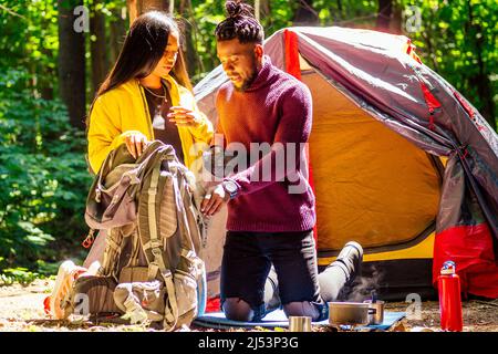 afroamerikanisches Mischvolk-Paar baut ein Zelt auf und hat eine Pause im Freien. Stockfoto