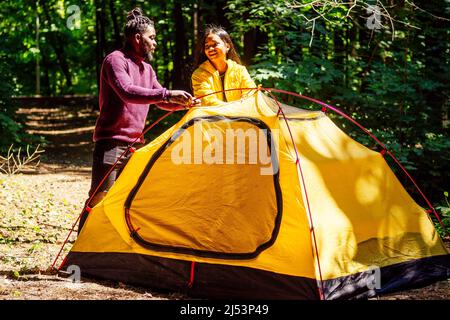afroamerikanisches Mischvolk-Paar baut ein Zelt auf und hat eine Pause im Freien. Stockfoto