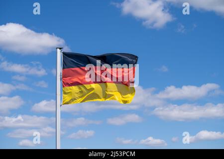 Die Nationalflagge Deutschlands winkt bei starkem Wind gegen den blauen Himmel mit verstreuten weißen Wolken Stockfoto