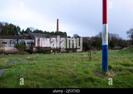 Rot weiß und blau bemalter Telegrafenmast und Blick auf den alten Kamin in der verfallenen Old Bleach Leinenfabrik in Randalstown County Antrim. Stockfoto