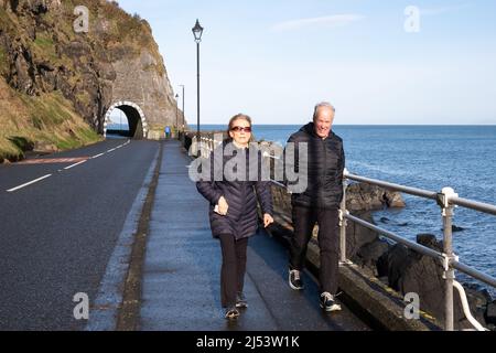 Ein Paar, das am Meer vor den Toren der Drains Bay an der Larne Coast in der Grafschaft Antrim Nordirland entlang geht. Stockfoto