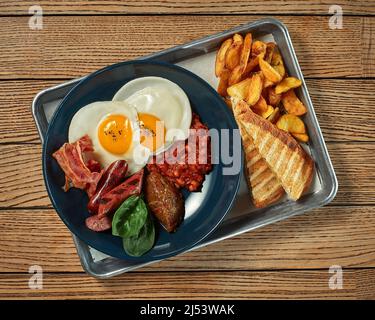 Frühstück mit Spiegeleiern, Kartoffeln, geschmorten Bohnen, Speck, Würstchen und Toast Stockfoto