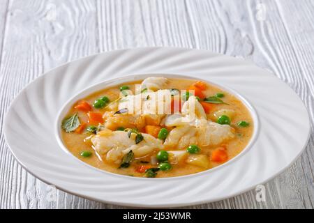 Fischsuppe mit Kabeljau, grünen Erbsen, Karotten, Kartoffeln und Milch auf pflanzlicher Basis, bestreut mit frischem Salbei, Thymian in einer weißen Schüssel, Nahaufnahme Stockfoto