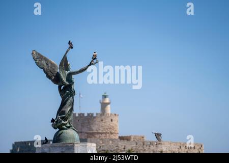 Angel Statue of Victory im Mandraki Hafen im Fokus und im Hintergrund die St. Nichola Festung. Stockfoto