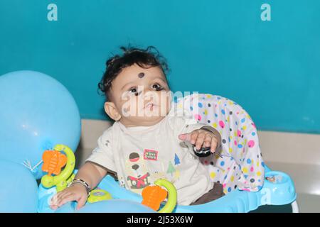 Chennai Tamilnadu, Indien . 02. Januar 2022.Nahaufnahme eines neugeborenen indischen Jungen, der in einem mit blauen Luftballons geschmückten Spaziergänger sitzt Stockfoto