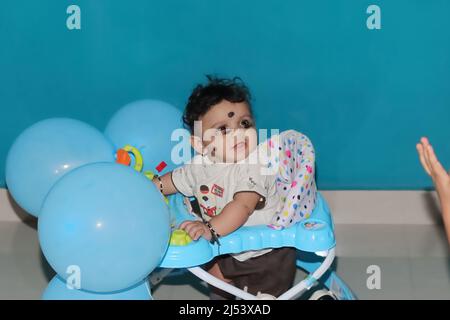 Chennai Tamilnadu, Indien . 02. Januar 2022.Nahaufnahme eines neugeborenen indischen Jungen, der in einem mit blauen Luftballons geschmückten Spaziergänger sitzt Stockfoto