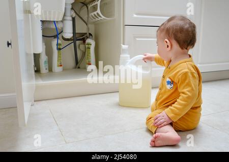 Kleinkind Baby Junge spielt mit Wasch-und Reinigungsmittel in einem offenen Küchenschrank. Probleme mit der Kindersicherheit im heimischen Zimmer, kleines Kind Stockfoto