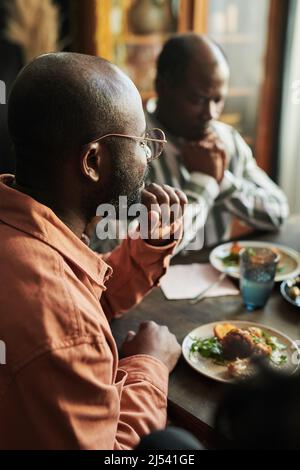 Afrikanischer Mann in einer Brille sitzt am Tisch und hat mit seiner Familie zu Hause zu Abend gegessen Stockfoto