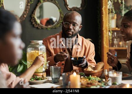 Afrikanischer Yung-Mann, der zu Hause am Tisch sitzt und mit seiner Familie zu Abend iß Stockfoto
