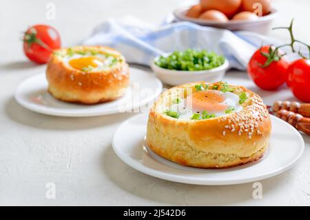 Gebackene Brötchen gefüllt mit Eiern und Speck auf Tellern auf weißem Hintergrund. Stockfoto